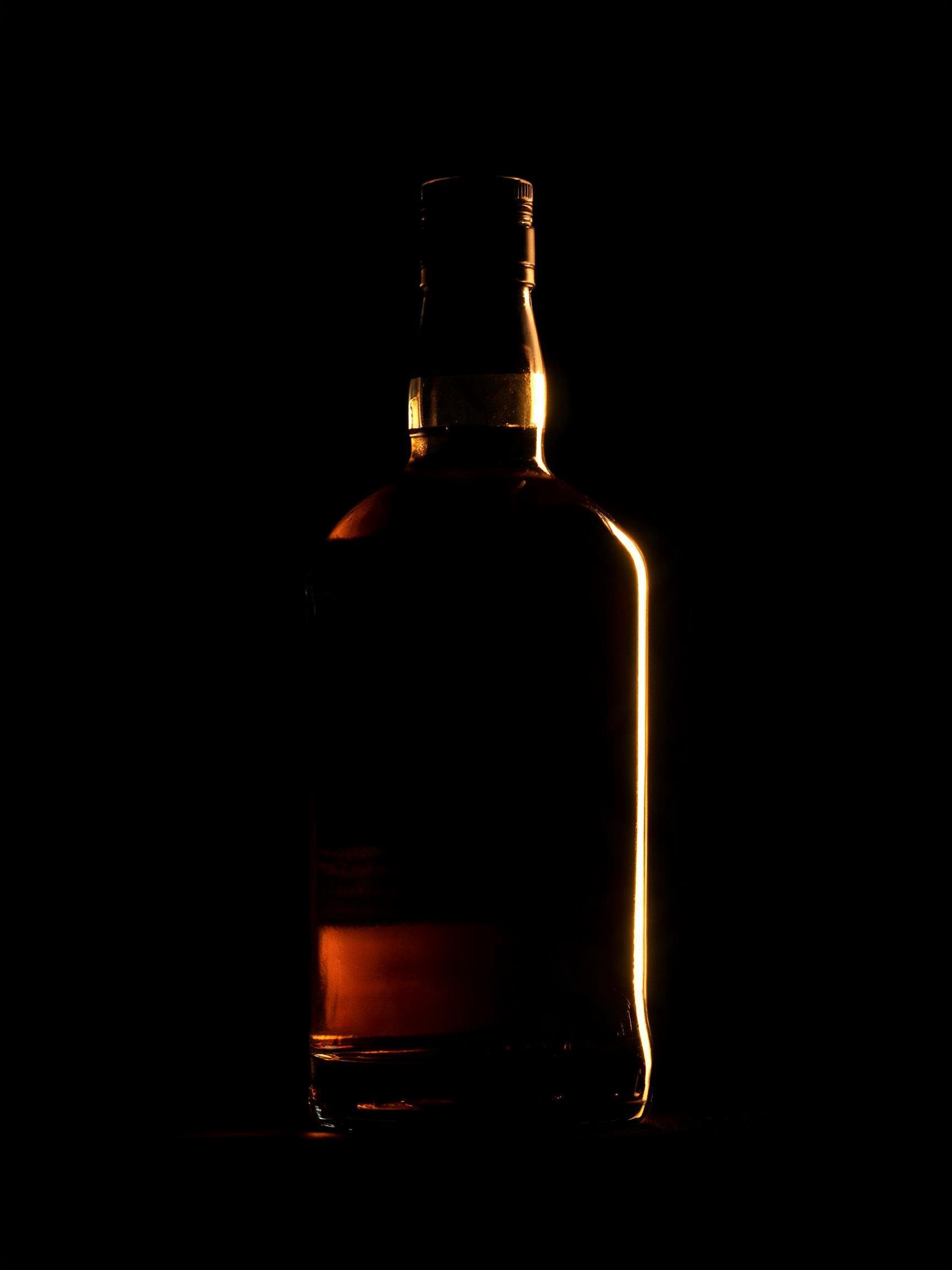 Mörk spritflaska i siluett mot varmt kontralljus